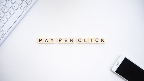 Pay per Click écrit en lettres de Scrabble sur support blanc-clavier-smartphone