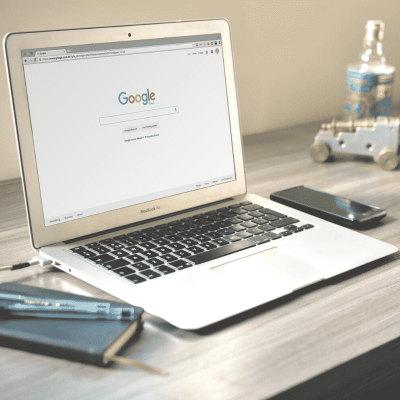 Open laptop displaying Google home page with diary and pen on wooden desk