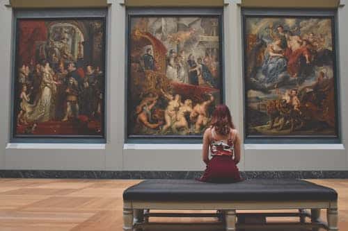 Woman sat facing 3 paintings in museum
